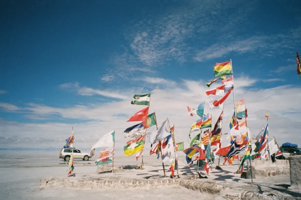 Flags of many nations flying over the Salar de Uyuni, a 4WD behind