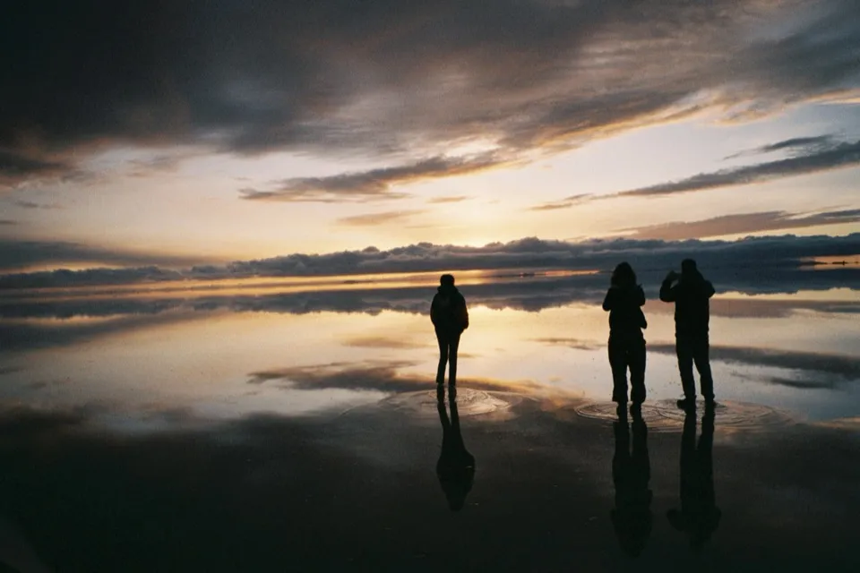 Three silhouettes on the flooded Salar de Uyuni at sunset