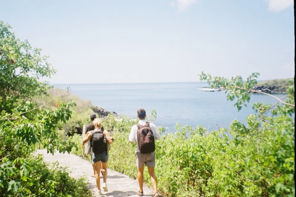Hikers with backpacks on a path down to a rocky cove on San Cristobal